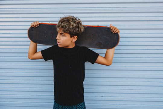 Boy holding his skateboard behind his head