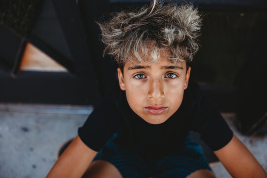 Boy with hazel eyes and bleached hair looking up at camera.