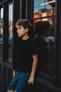 Boy leaning against a black wooden and glass wall.