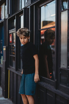 Boy standing on his skateboard leaning against a black wooden wall.