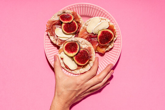 Hand of woman picking up rice cake with serrano ham, cheese and fig slices