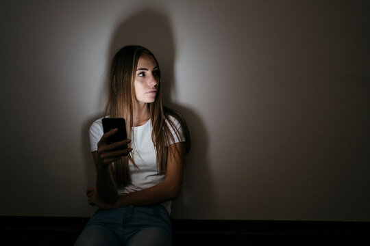 Young woman at home sitting on floor using cell phone in the dark