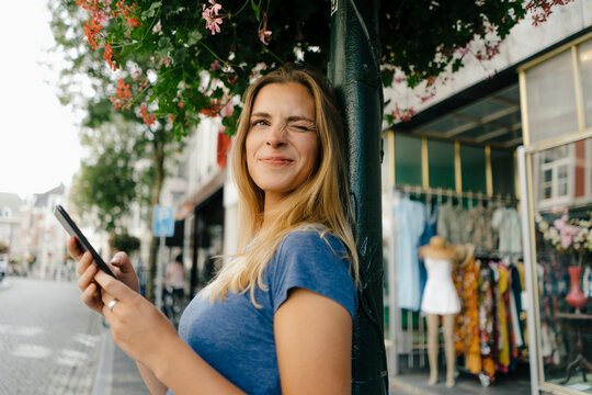 Netherlands, Maastricht, smiling young woman with cell phone in the city twinkling