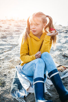 Portrait of girl with plaits sitting on the beach in autumn eating an apple