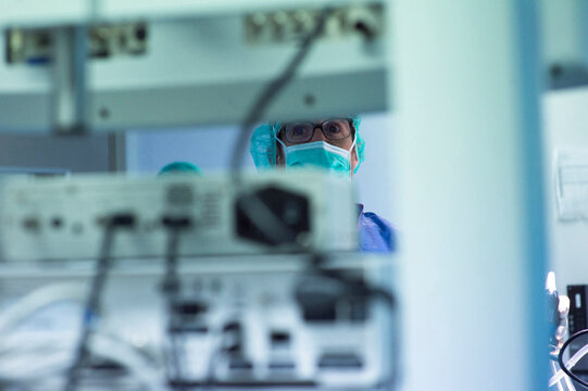 Focused male surgeon looking at monitoring equipment while operating in ICU