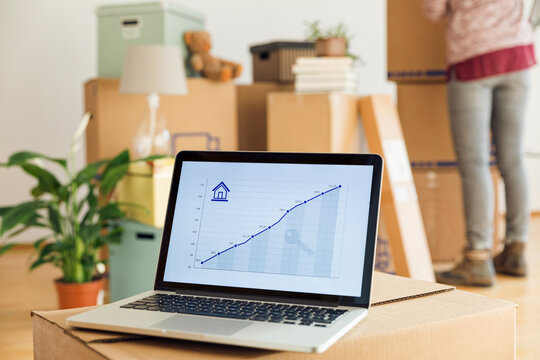 Rising line graph on laptop screen in front of cardboard boxes in a new home