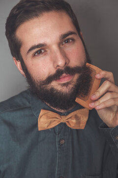 Man combing his beard with a wooden comb, wearing denim shirt and cork bow tie