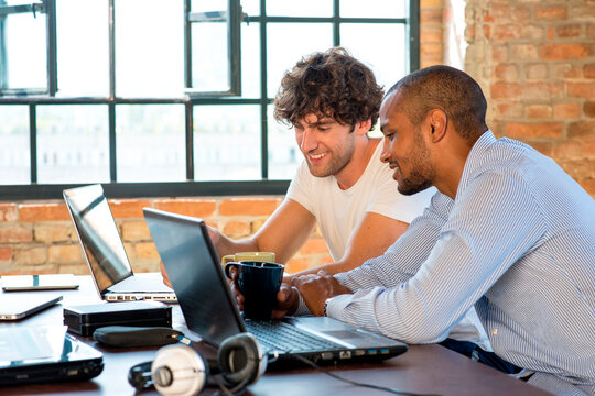 Two young businessmen working together in co-working space, using laptops