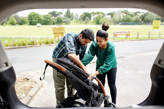 Indian couple fixing pram behind car boot in the parking space