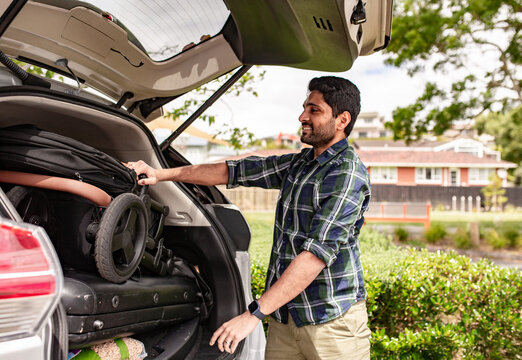Indian man with a beard unloading the pram from the car boot