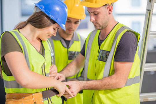 Construction worker helping colleague with tool belt