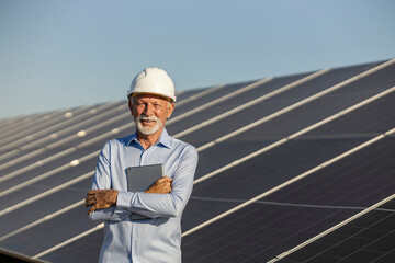 Senior Male Environmentalist Standing Confidently Near Solar Panels Holding Tablet