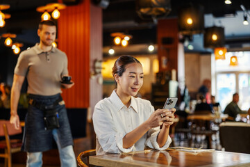 Woman using phone in restaurant, waiter serving coffee