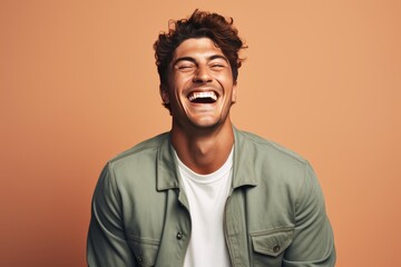 Fototapeta premium Young man standing against a peach background laughing with closed eyes