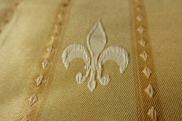 Close shot of beige fabric with embroidered fleur de lis symbol © Anna