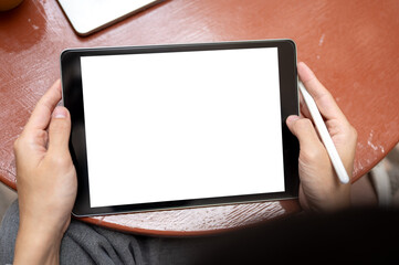Top view of hands holding white screen tablet and stylus pen sitting on chair at table on tile...