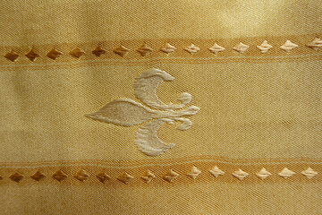 Surface of beige fabric with embroidered fleur de lis symbol © Anna
