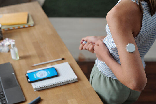Person with insulin patch using glucose meter app at desk