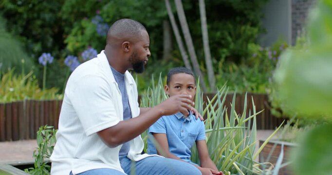 African American father and son sitting on bench, father placing hand, speaking to reassure