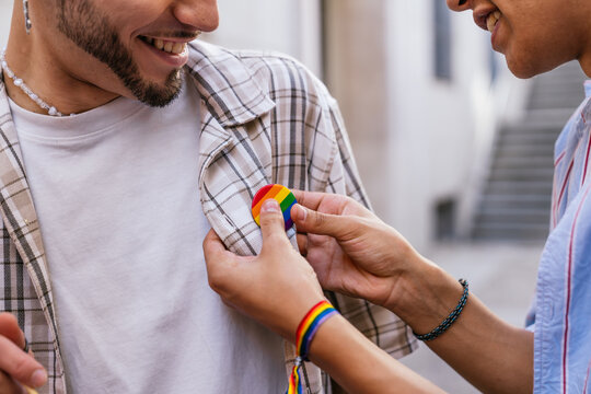 Someone's hands putting a colorful lgbtq plus rainbow pride flag pin on another person's plaid shirt, showing support for the community