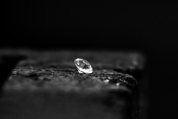 Single gemstone rests on a rough surface in deep shadow. Facets catch a cold gleam and suggest value and promise while the quiet emptiness around it feels timeless focused and still