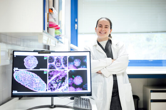 Scientist in laboratory standing beside monitor with microscopy images