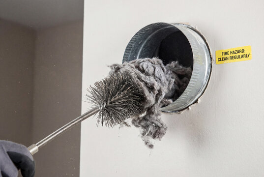 Cleaning clogged dryer vent duct with wire brush pulling out thick grey lint fire hazard
