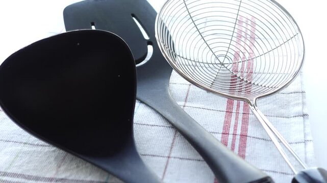 Close up of cooking utensils including a slotted spoon and ladle on a checkered cloth