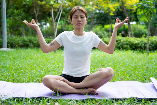 Beautiful young woman practicing Padmasana on yoga mat outdoors, space for text.