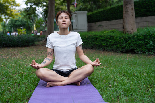 Beautiful young woman practicing Padmasana on yoga mat outdoors, space for text. Lotus pose