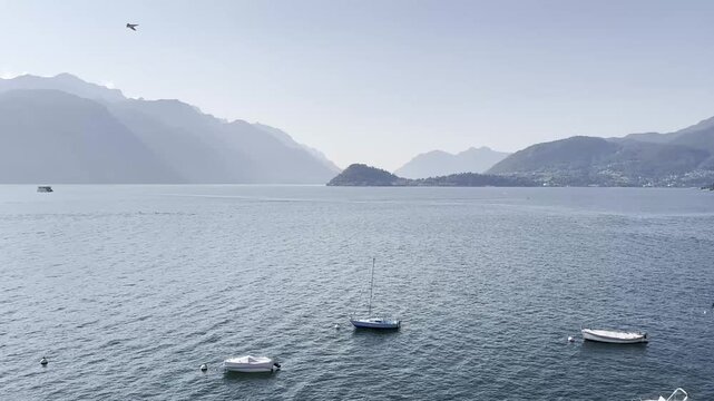 Movimiento panor&aacute;mico suave de derecha a izquierda mostrando la costa de Lake Como, con villas italianas en tonos pastel, peque&ntilde;os embarcaderos con barcas amarradas y monta&ntilde;as verdes al fondo. El agua