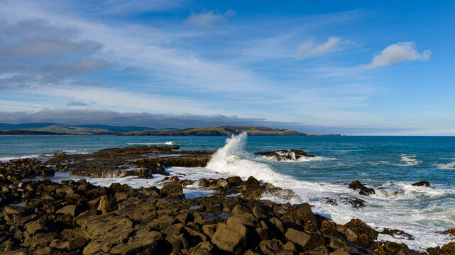 view of waves breaking and on a rocky shore with blue sky and wispy clouds