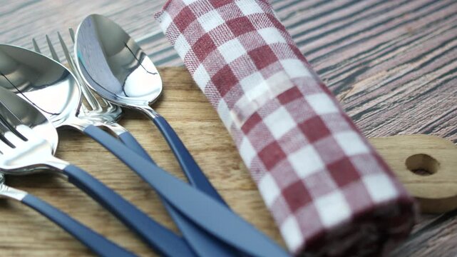 Close up of blue and silver silverware on wooden board with checkered napkin for dining table presentation