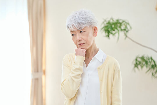 部屋で悩むアジア人シニア女性
