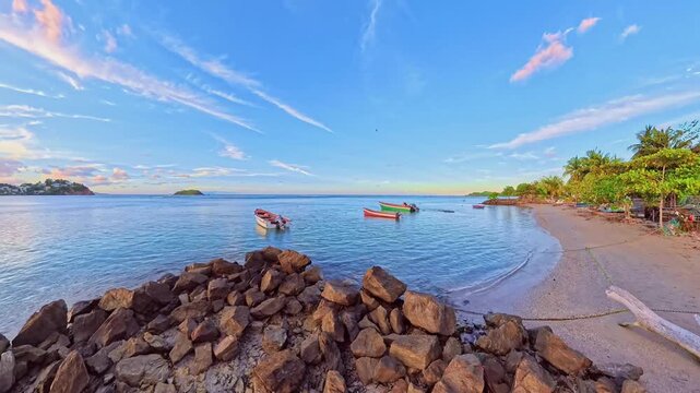 Time-lapse:panoramic colorful sunset sky reflecting on tranquil bay of Tartane beach, with small fishing boats moored along palm-fringed coast and rocky shore of Martinique, French Antilles, Caribbean