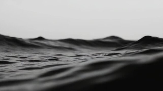 Dark water undulating in rhythmic patterns, creating an abstract liquid landscape with a minimalist and moody atmosphere under an overcast sky, evoking concepts of nature, calmness, and movement