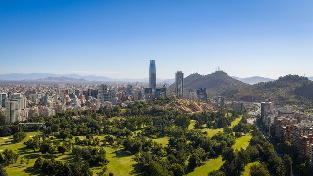 Aerial view of Santiago de Chile skyline with green park and distant Andes mountains under a clear blue summer sky.