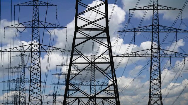Wolken im Zeitraffer hinter den Stromleitungen und Strommasten einer Starkstrom &Uuml;berlandleitung - FOTOMONTAGE