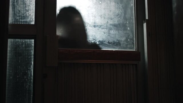 Silhouette of person knocking on door behind opaque glass