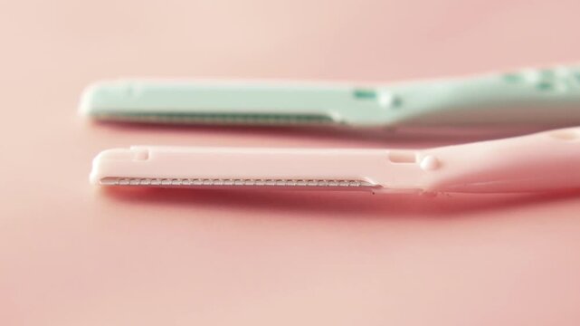 Close up motion of two dermaplaning razors for facial hair removal on a pink background
