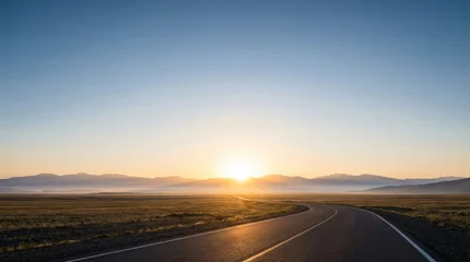 Fototapeten Beige A winding asphalt road leads across a vast open landscape towards a bright sunrise over distant mountains  © Mimie