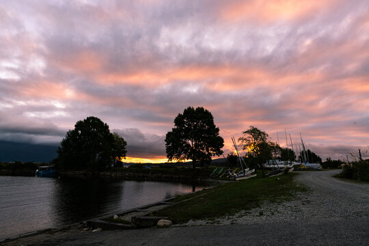 Sailing boats on the banks of a lake in the sunset with pink coloured cloud patterns