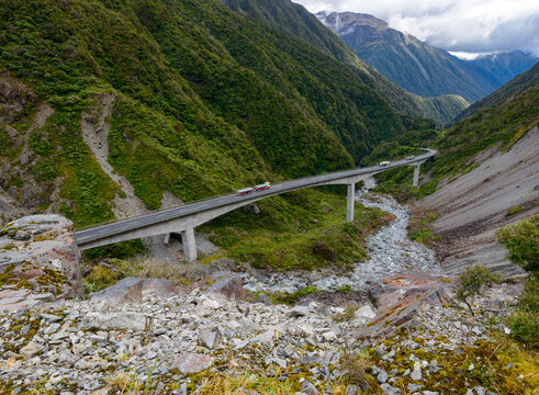 Looking down on vehicles travelling along a bridge through a pass in the mountains