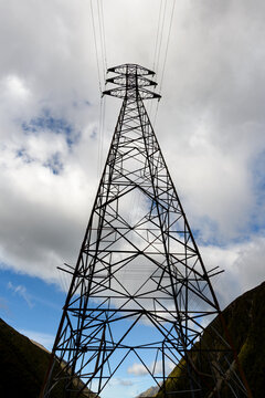 Looking up at an electrical transmission tower silhouetted against the clouds.