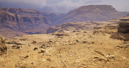Vast desert landscape reveals rocky terrain and imposing mountain ranges under a clear sky. Dry ground stretches towards distant peaks, creating a serene natural environment. © icetray