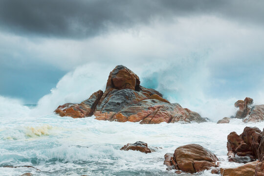 Large ocean waves crashing over coastal rock formations under a dark stormy sky
