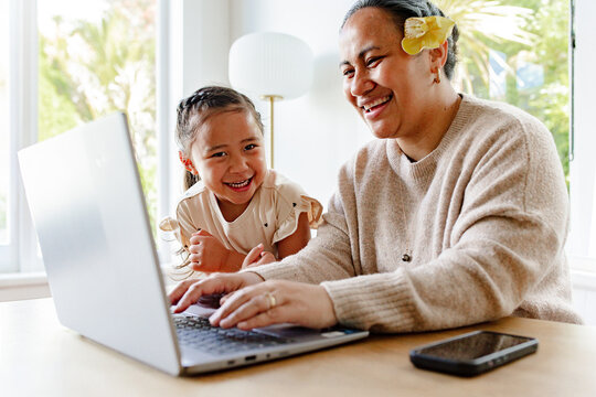 Young girl smiling with mum while working on her laptop