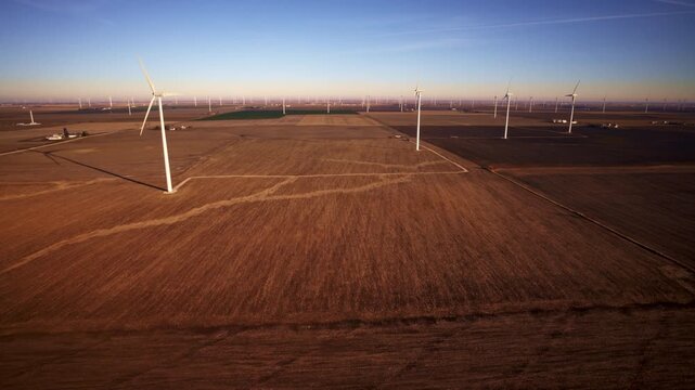 Gradual aerial circle of wind turbines rising above farmland