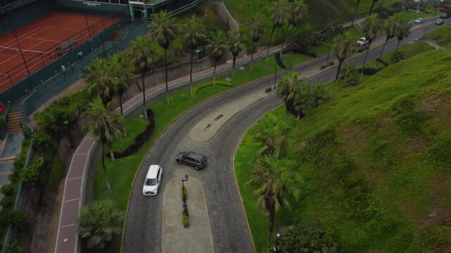 Aerial shot of road called "Bajada Balta" which goes under bridge called "Puente Villena" and goes down to the pacific ocean beach. Drone hovers and pans. Located in Miraflores district of Lima, Peru.