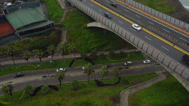 Aerial shot of a bridge called "Puente Villena" built over a road called "Bajada Balta" which leads down to the beach of the pacific ocean. Drone hovers and tilts up. Located in Miraflores, Lima, Peru